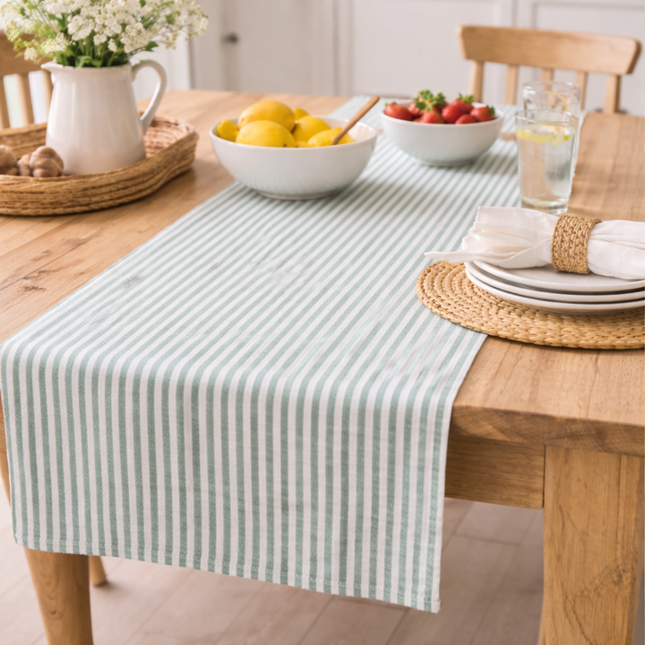 Table setting with a striped table runner, bowls of fruit, and a vase on a wooden table.