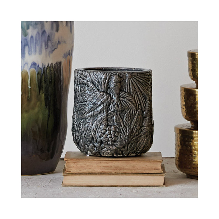 Decorative ceramic pot with textured design on a stack of books, with other decorative items in the background.