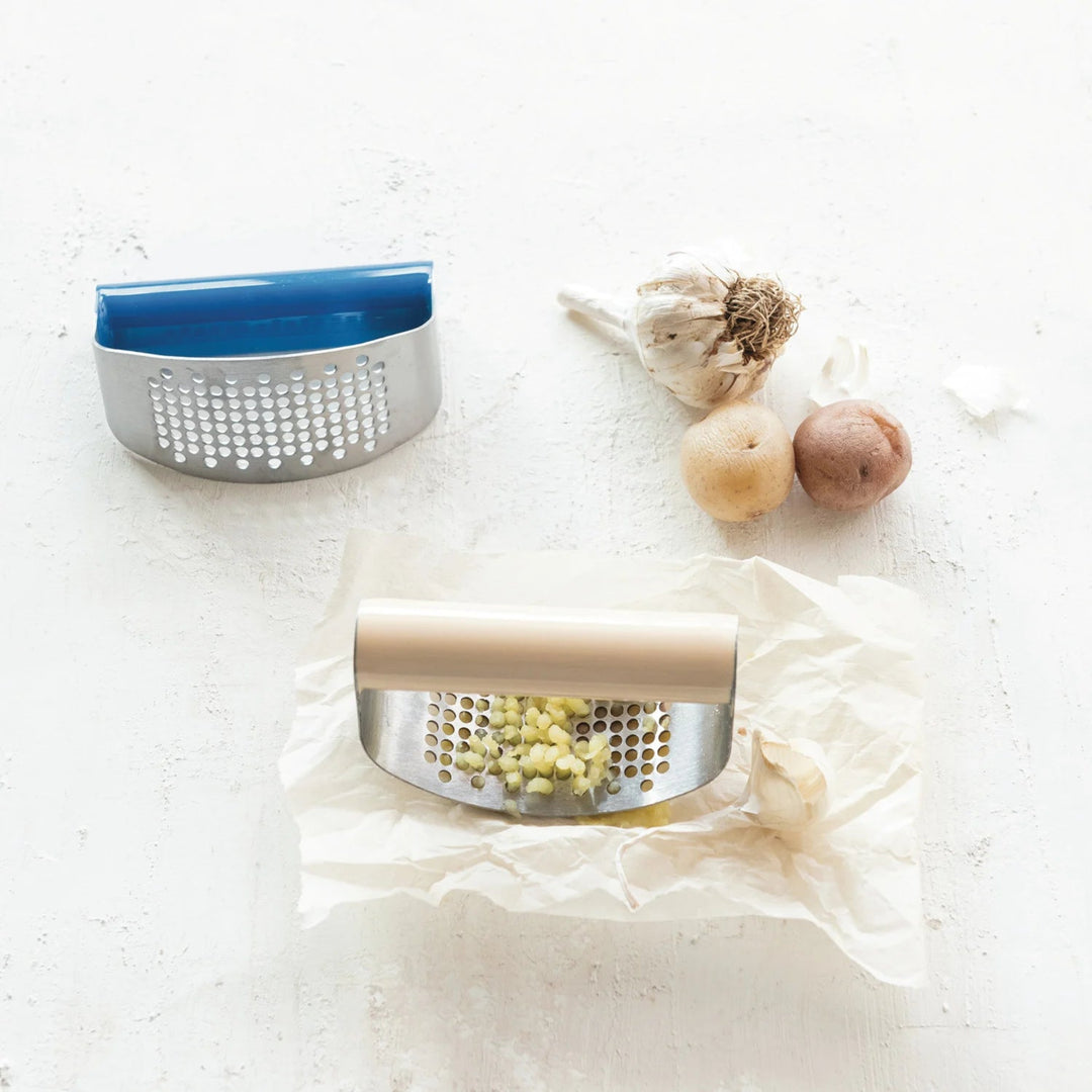 Metal garlic press with garlic cloves on a white surface