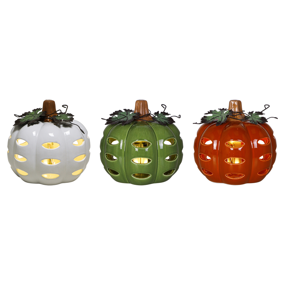 Three decorative ceramic pumpkins in white, green, and orange, each with carved cutouts that reveal warm yellow light inside, shown on a plain white background.