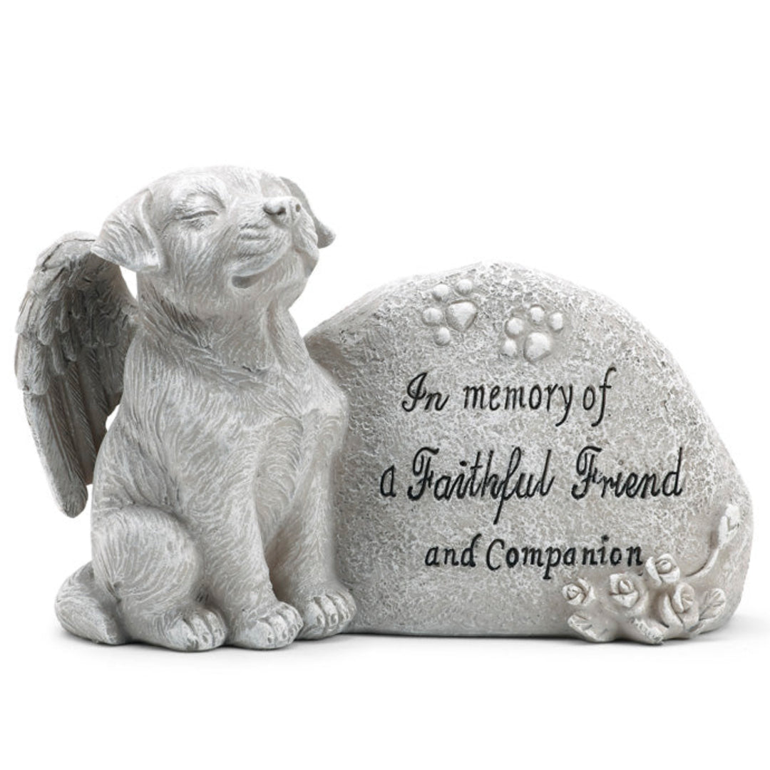 Memorial sculpture of a dog with angel wings and a stone with engraved text on a white background