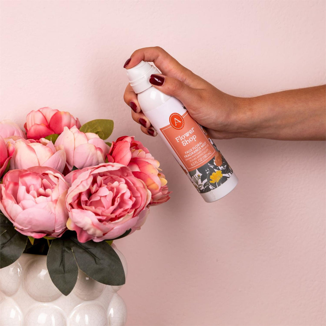Hand holding a floral spray bottle with pink flowers in the foreground