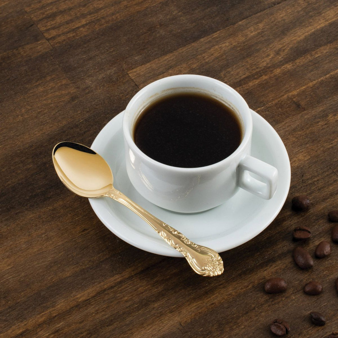 White coffee cup with dark coffee, gold spoon, and scattered coffee beans on a wooden surface