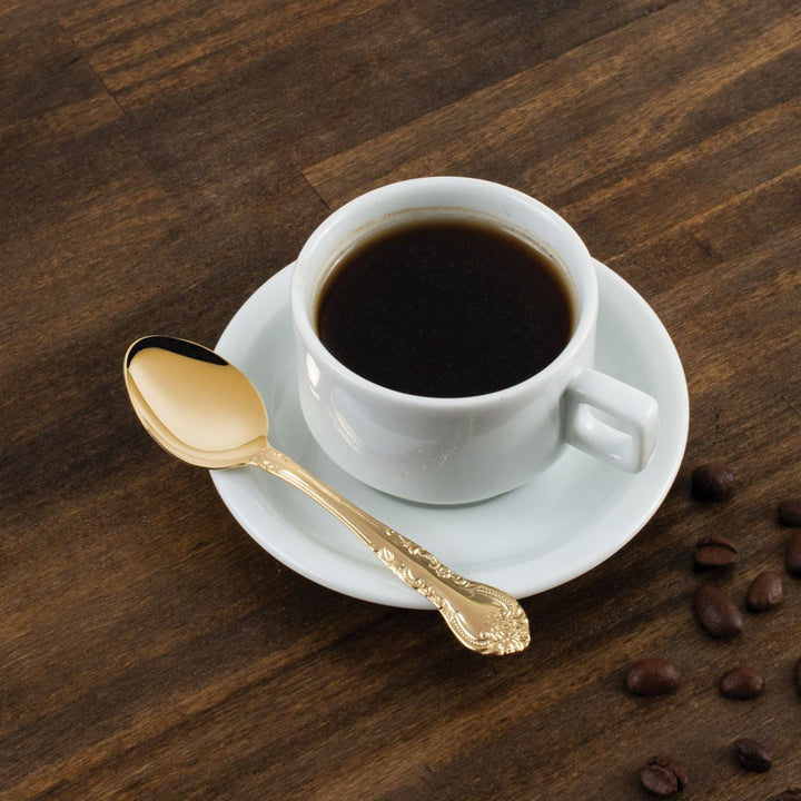 White coffee cup with dark coffee, gold spoon, and scattered coffee beans on a wooden surface