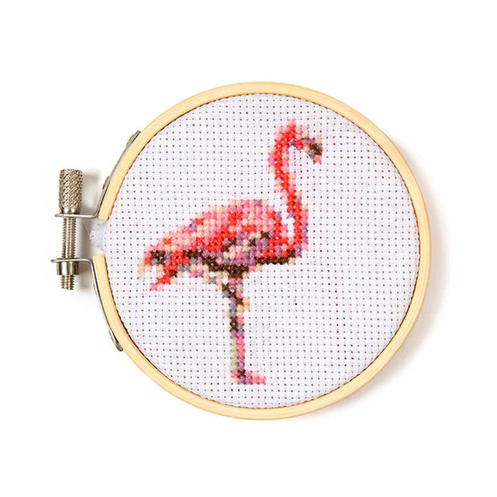 Cross-stitched flamingo design in a wooden hoop on a white background