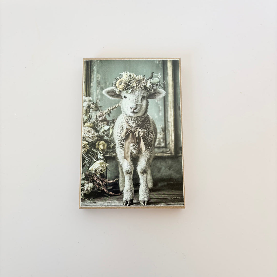 Framed artwork of a lamb with a floral crown on a white wall
