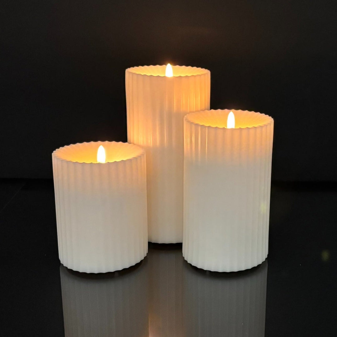 Three ribbed candles with a warm glow on a reflective black surface.
