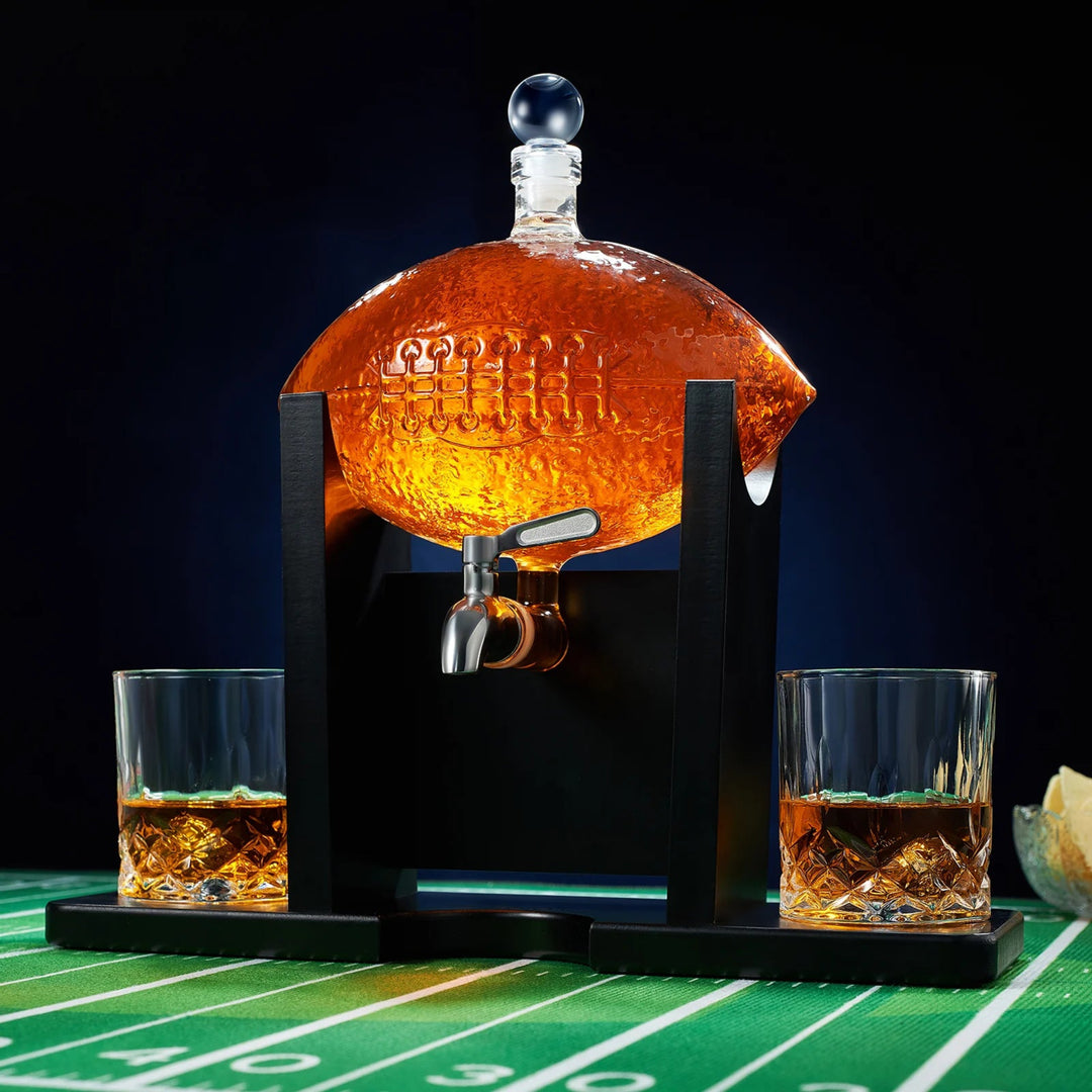 A football-shaped decanter set with two whiskey glasses, displayed on a table with a football field background.