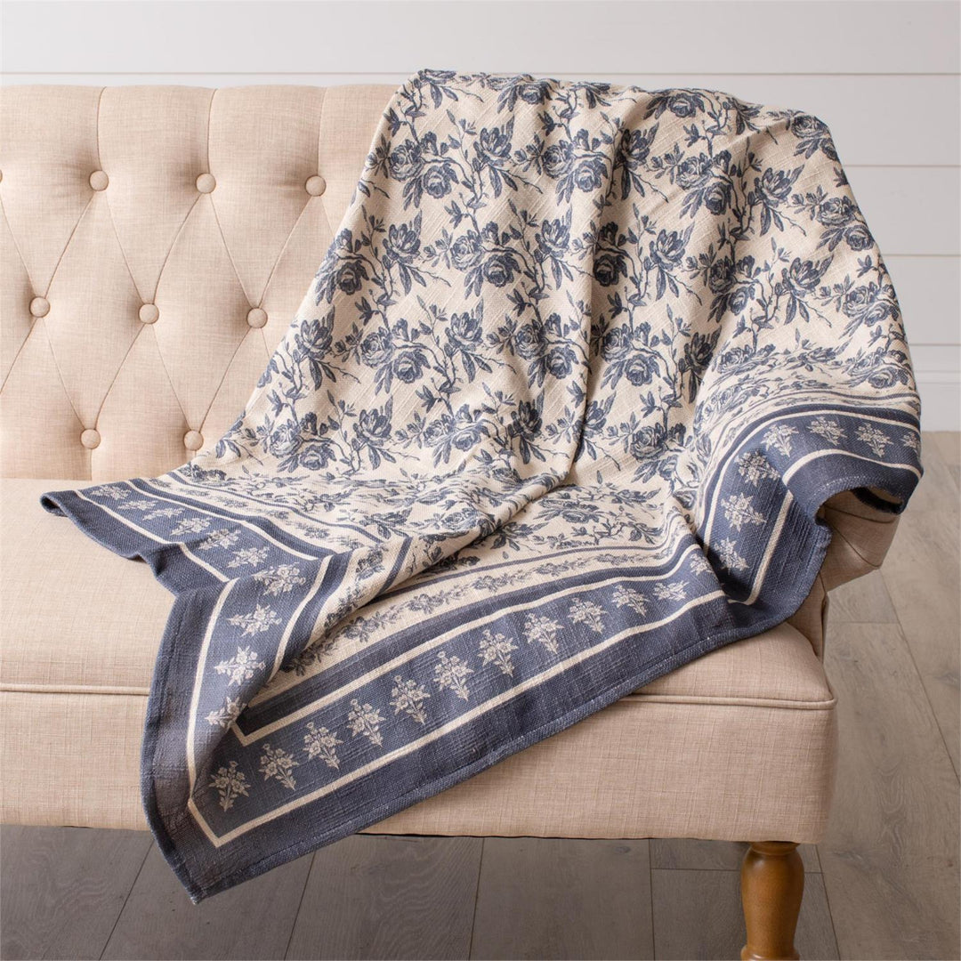 Blue floral patterned throw blanket draped over a beige sofa.