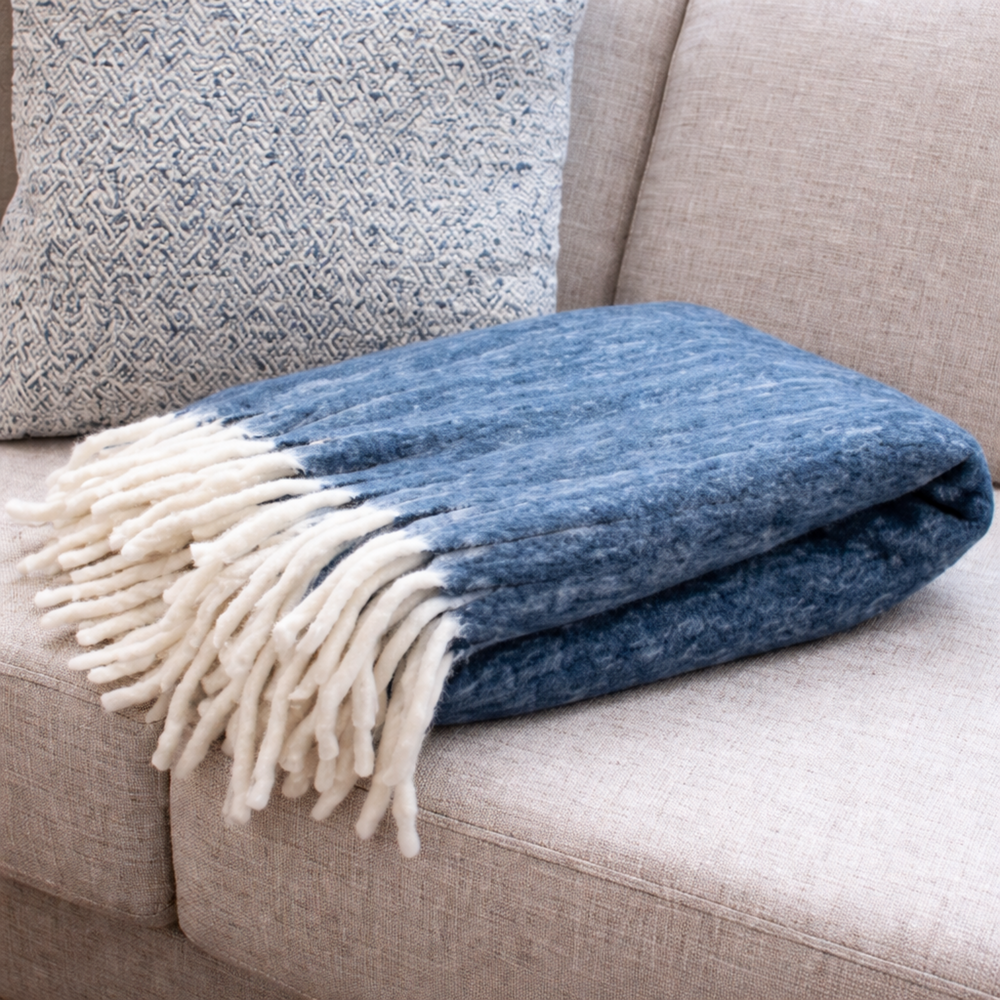 Blue blanket with white fringe draped over a beige couch