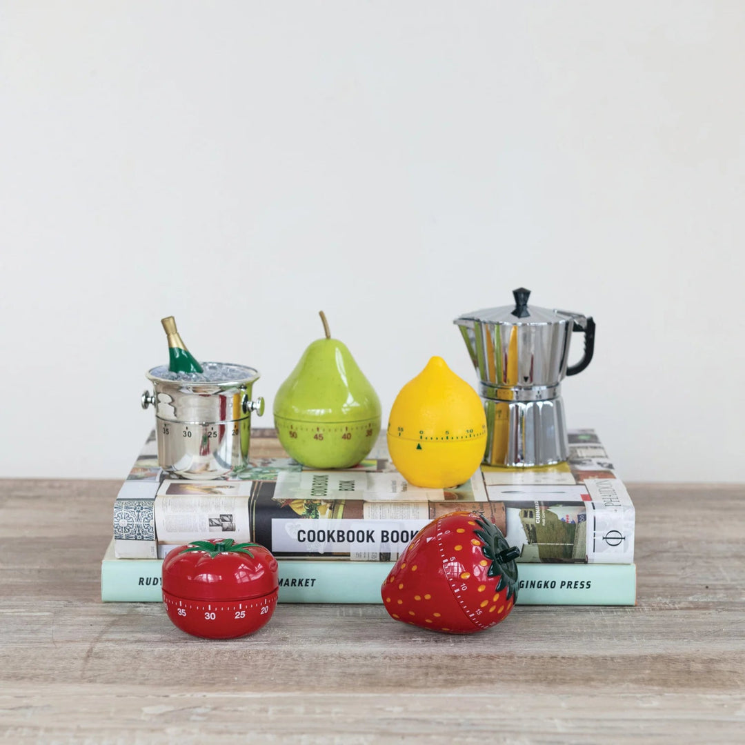 Decorative kitchen timers shaped like a tomato, strawberry, lemon, pear, and coffee pot on books with a white background.