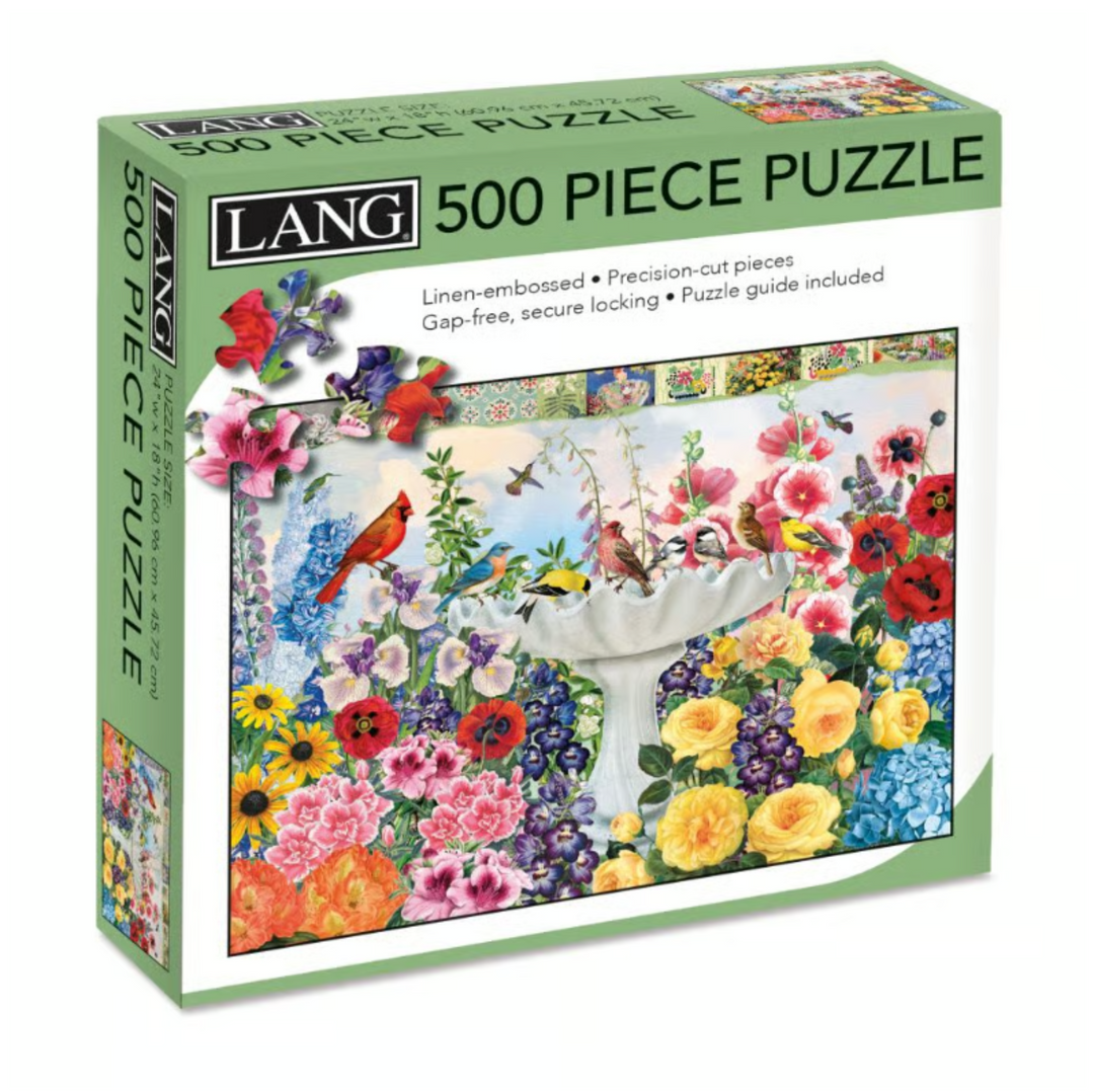 Lang 500-piece jigsaw puzzle box featuring a colorful garden scene with flowers, birds, and a white stone garden bed. The green and white packaging displays the Lang brand name and product details.