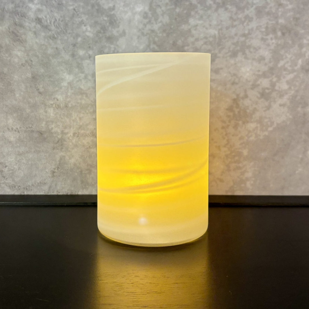 Glass lamp with a warm glow on a dark surface against a gray textured wall