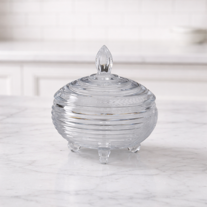 Clear glass candy dish with ribbed design on a marble surface