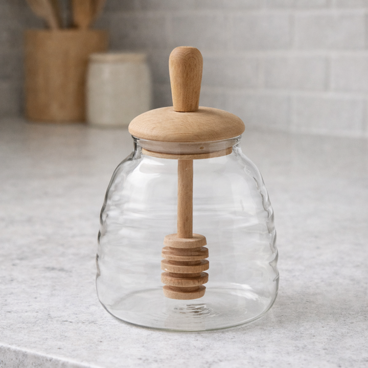Glass jar with wooden lid and honey dipper on a kitchen counter
