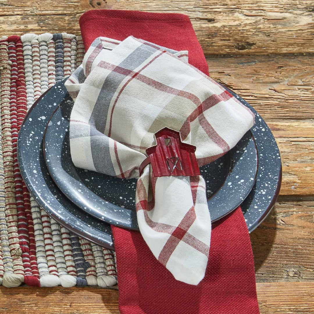 Plaid napkin with a red napkin holder on a stack of gray plates on a wooden surface.