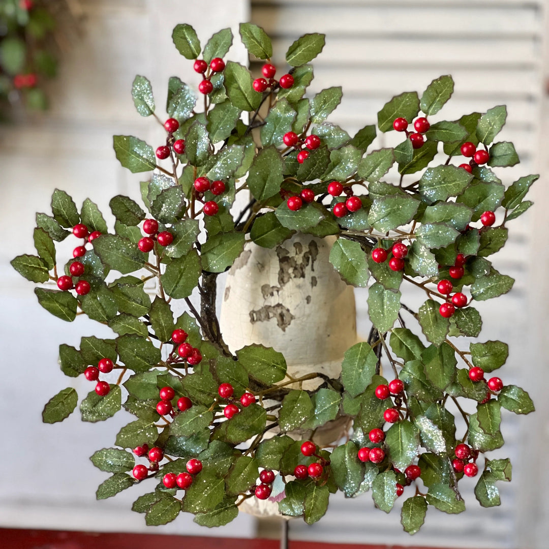 Decorative wreath with red berries on a stand against a neutral background