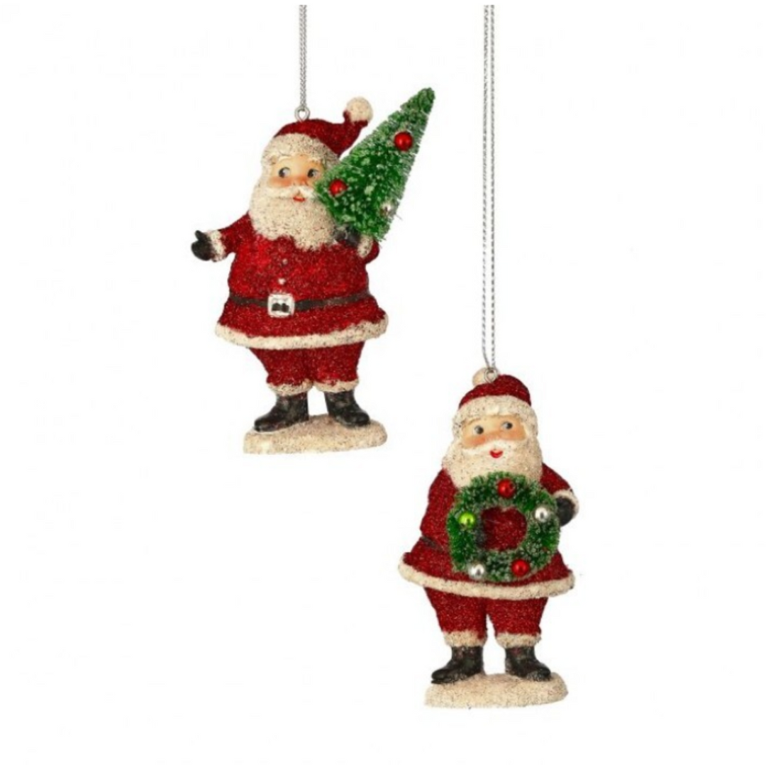 Two glittery Santa Claus Christmas ornaments hanging against a white background. One Santa holds a small green Christmas tree, and the other holds a green wreath with red ornaments.