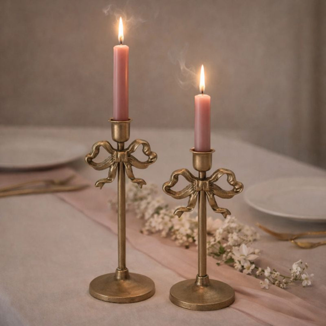 Two brass candlesticks with pink candles on a table setting.