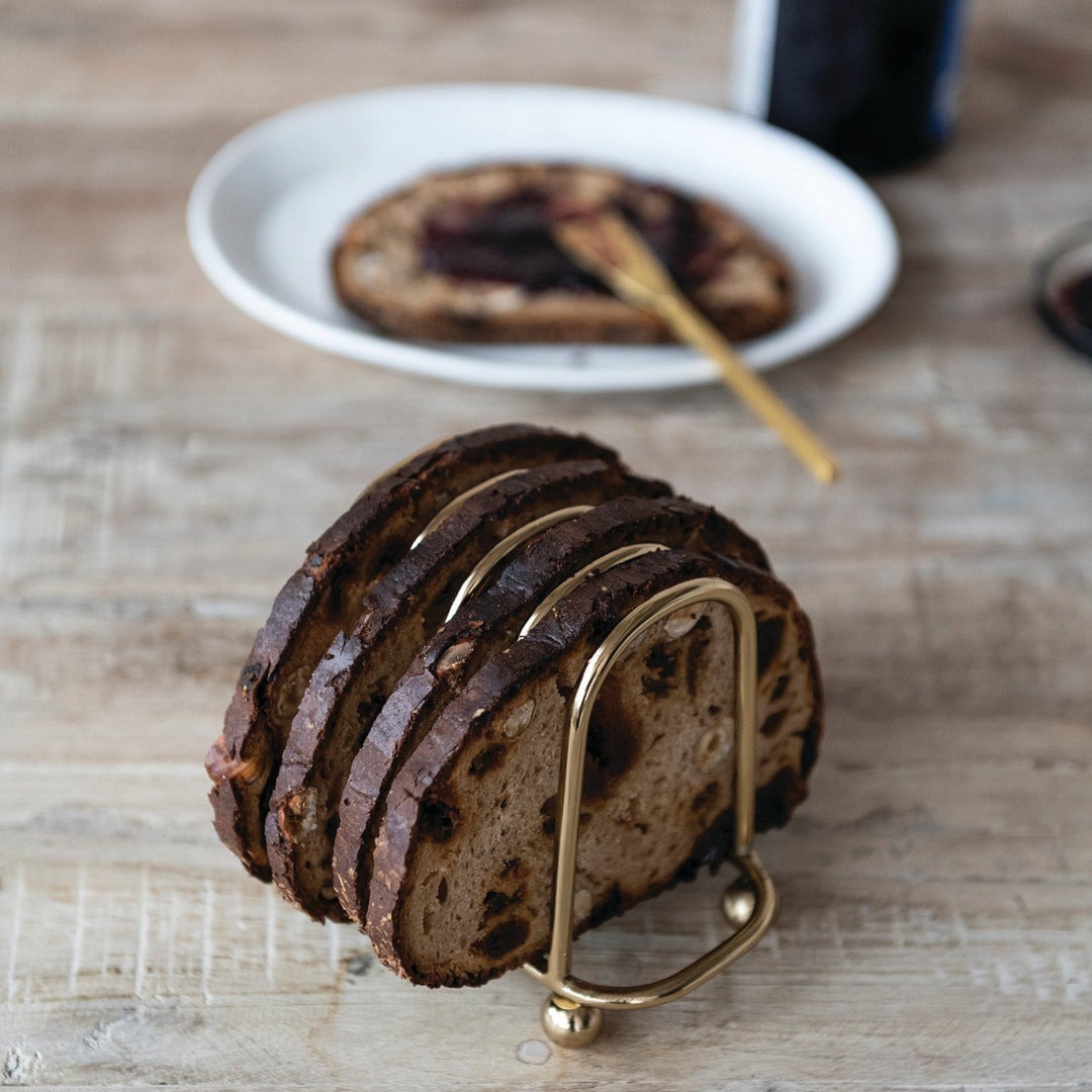 Gold Finished Toast Rack with toasted bread displayed. plate with knife and toast in the background. wooden tabletop 