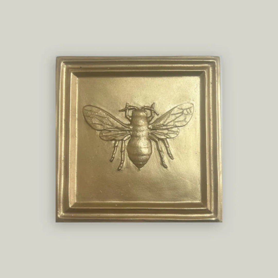 Gold-framed wall art with a bee design on a light gray background