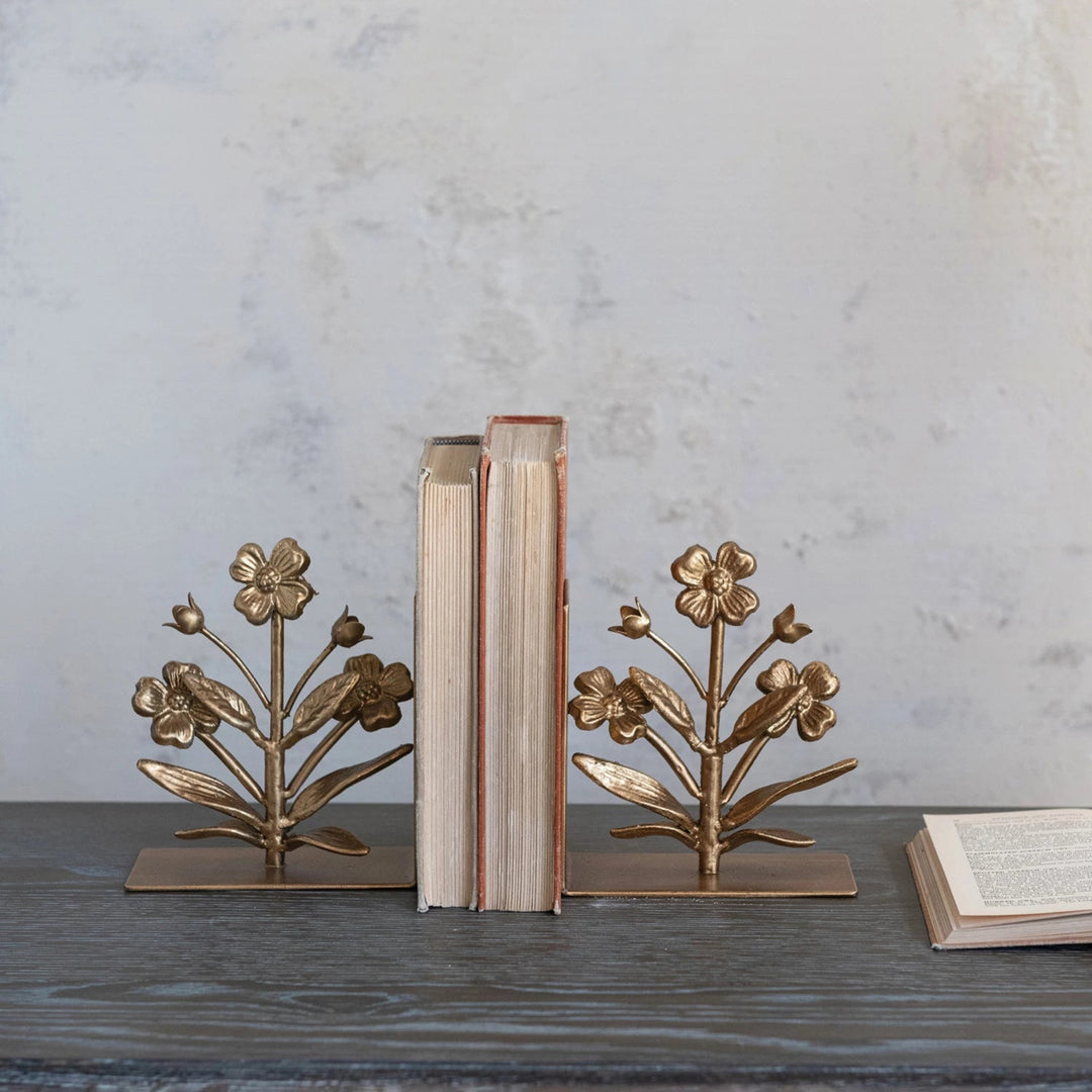 Bronze floral bookends holding books on a wooden surface with a gray marble background