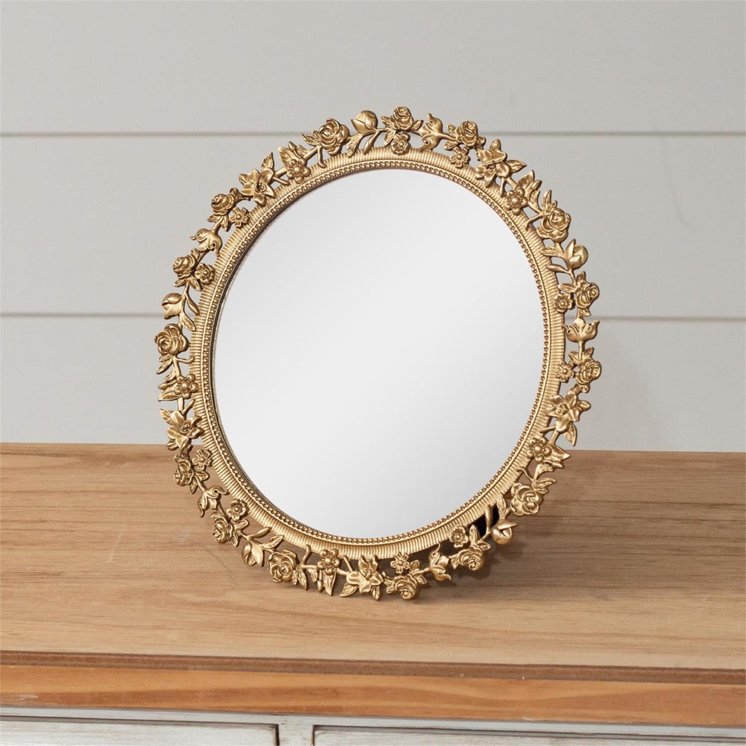 A golden floral framed mirror with a pewter frame and glass, displayed on a wooden surface.