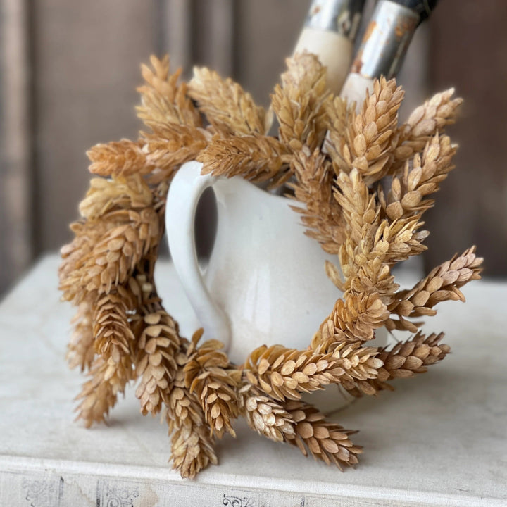 White mug with decorative wheat wreath on a wooden surface