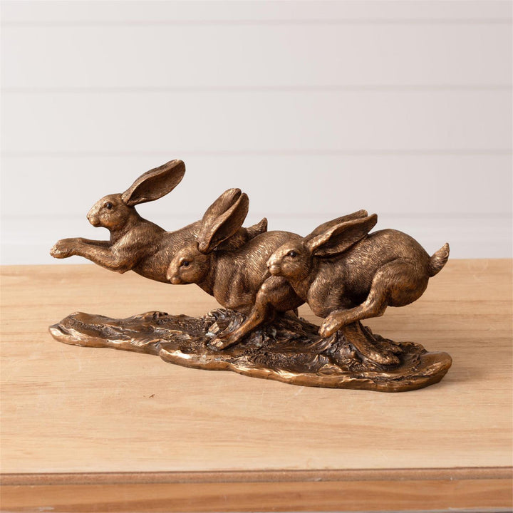 Bronze sculpture of three rabbits on a wooden surface with a light gray background