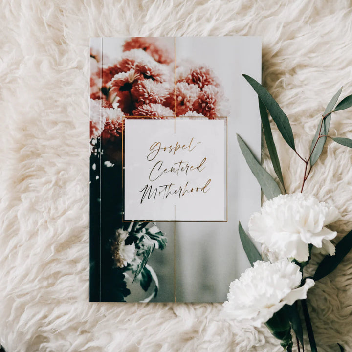 Book titled 'Gospel Centered Motherhood' on a fluffy white surface with flowers.