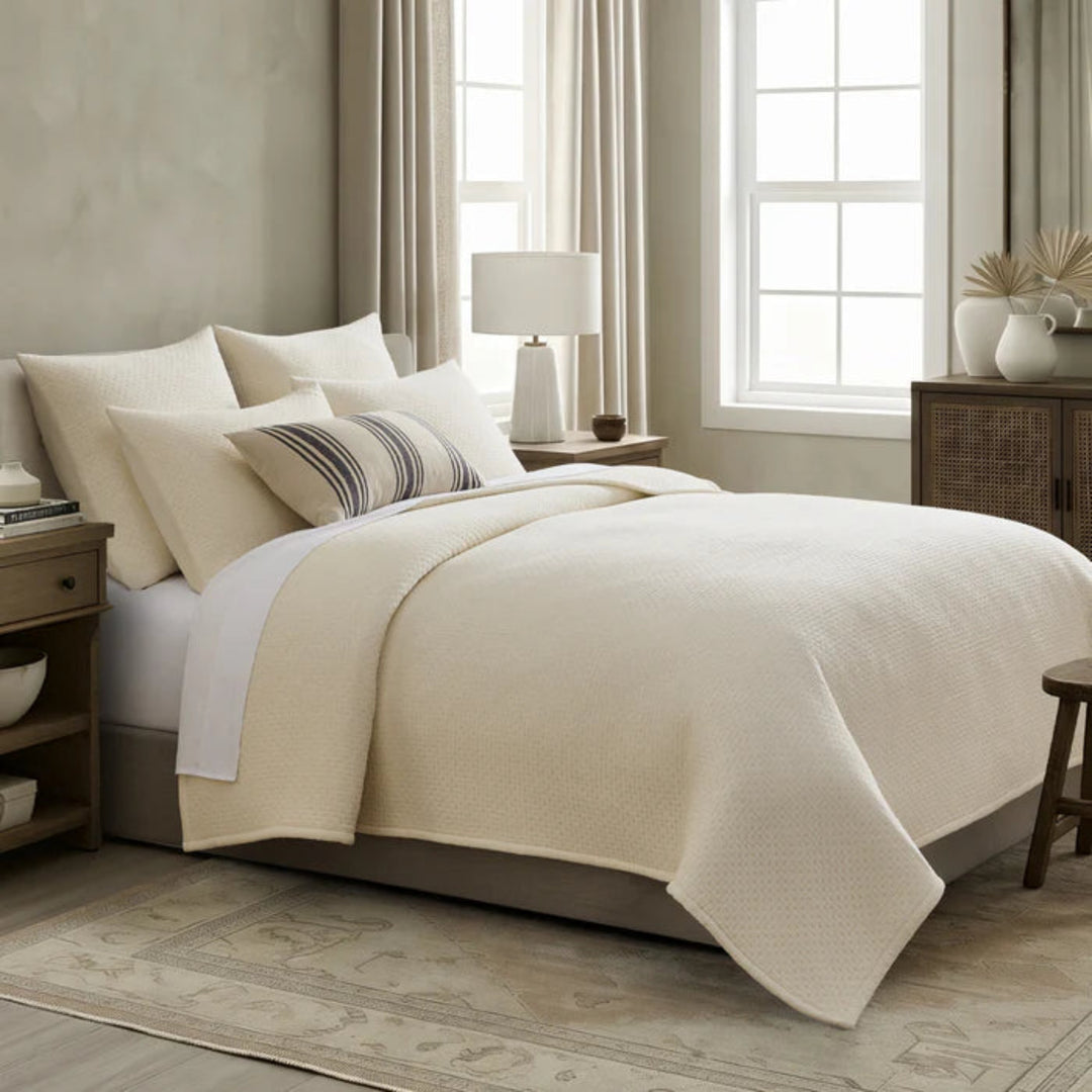 Neatly made bed with beige comforter and pillows in a bedroom setting.