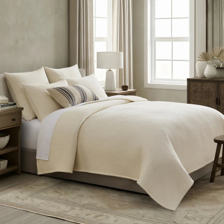 Neatly made bed with beige comforter and pillows in a bedroom setting.