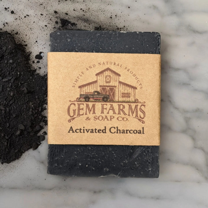 Bar of activated charcoal soap from Gem Farms Soap Co. on a marble surface with some charcoal powder.