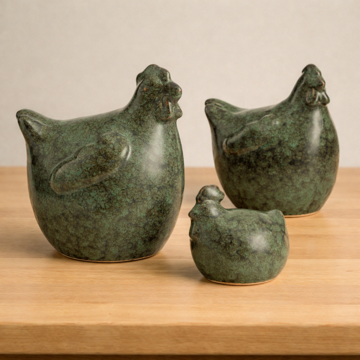 Three green ceramic chicken sculptures on a wooden surface with a beige background