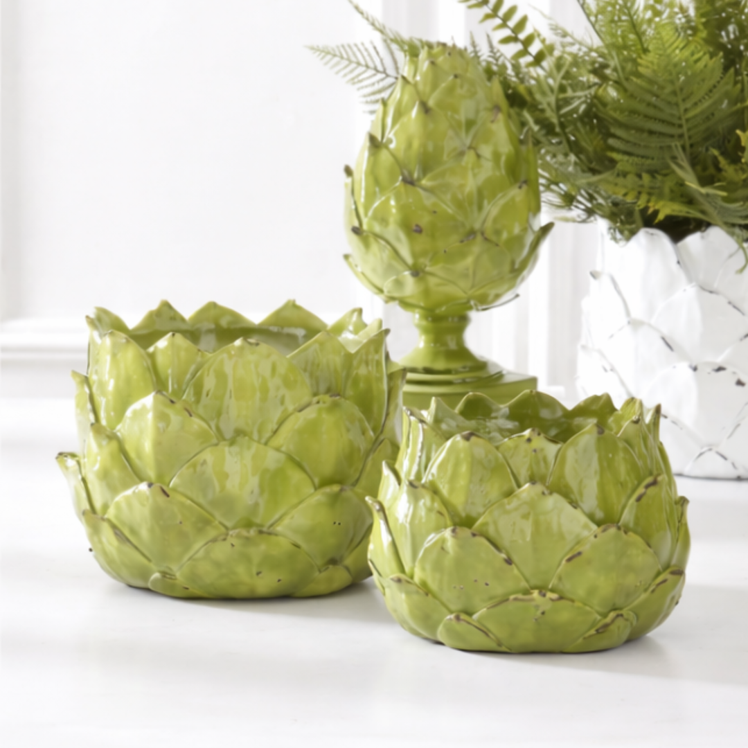 Three green artichoke-shaped planters on a white surface with a blurred background