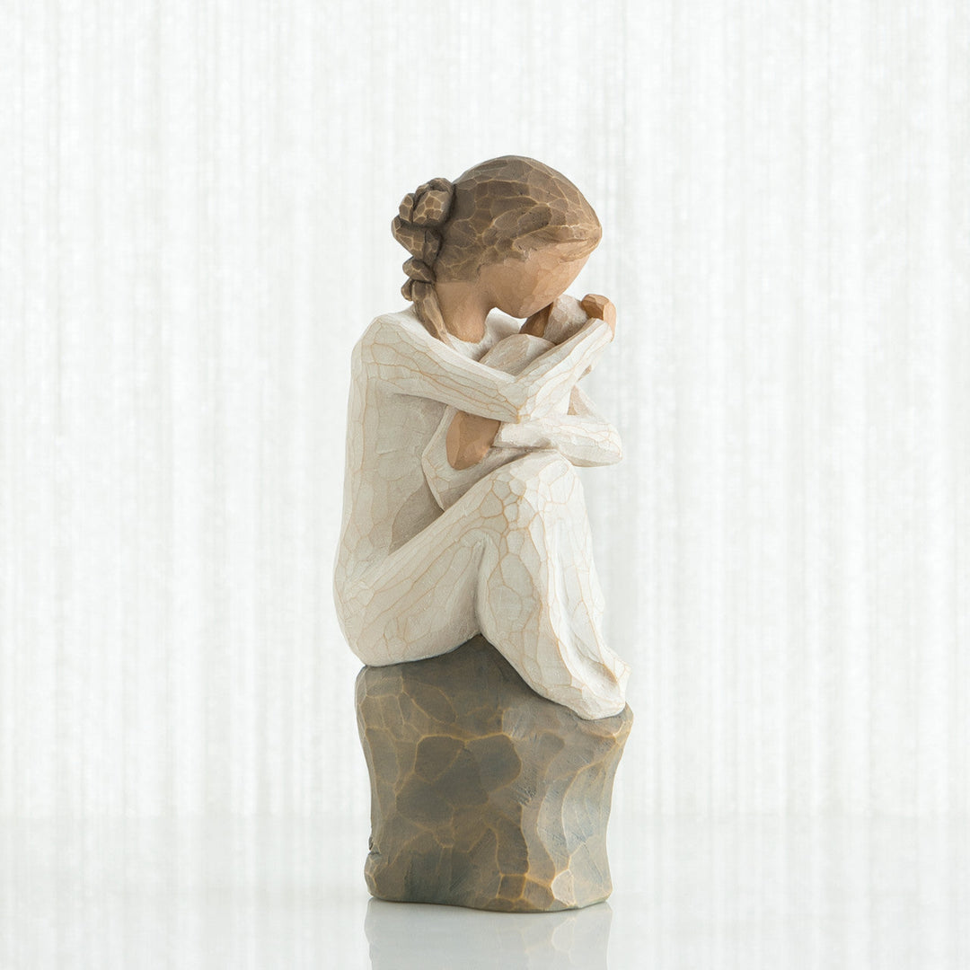 Statue of a woman sitting with her head in her hands against a white curtain background