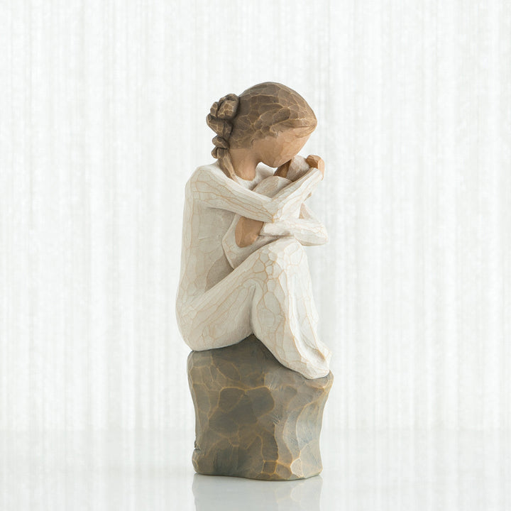Statue of a woman sitting with her head in her hands against a white curtain background