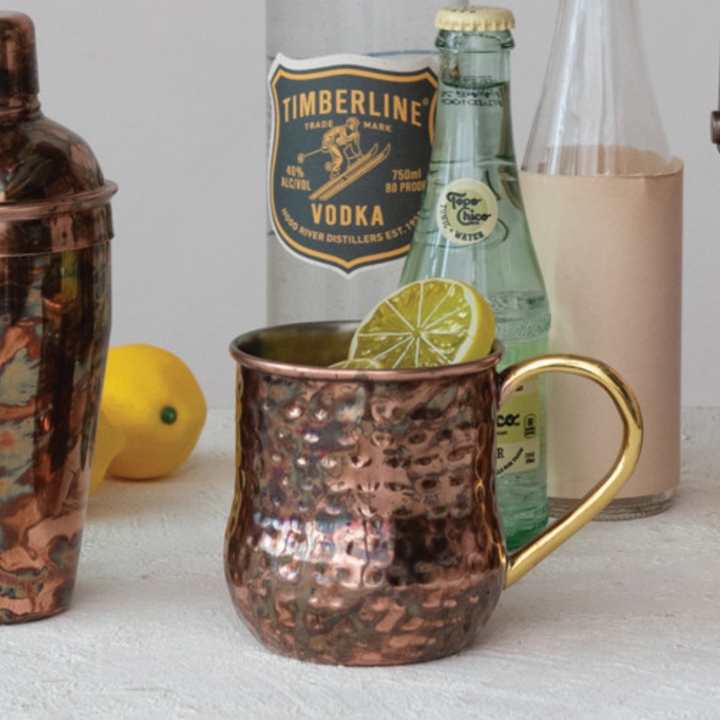 Copper mug with a drink and lime wedge, next to bottles of Timberline Vodka and a green bottle.