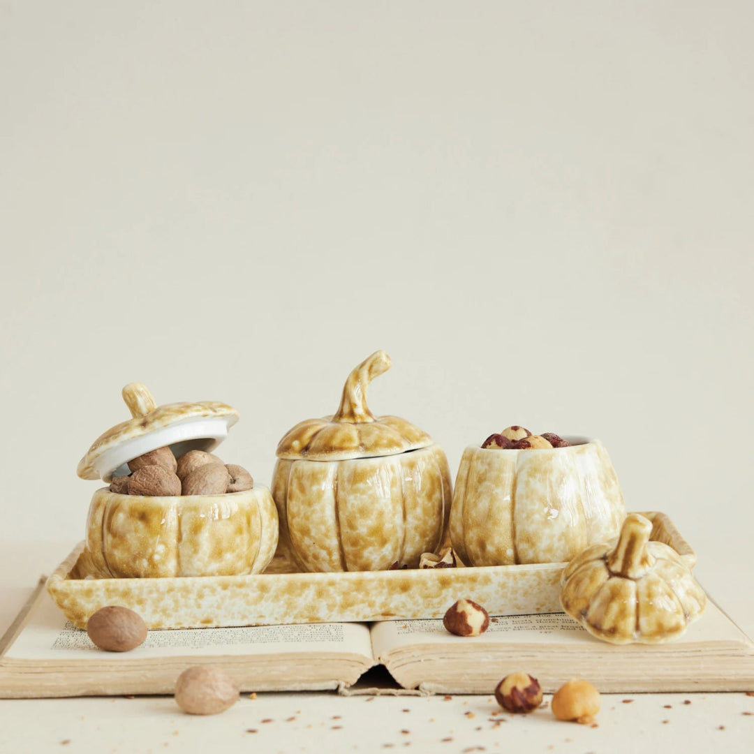 Decorative pumpkin-shaped containers with lids on a wooden tray against a light background