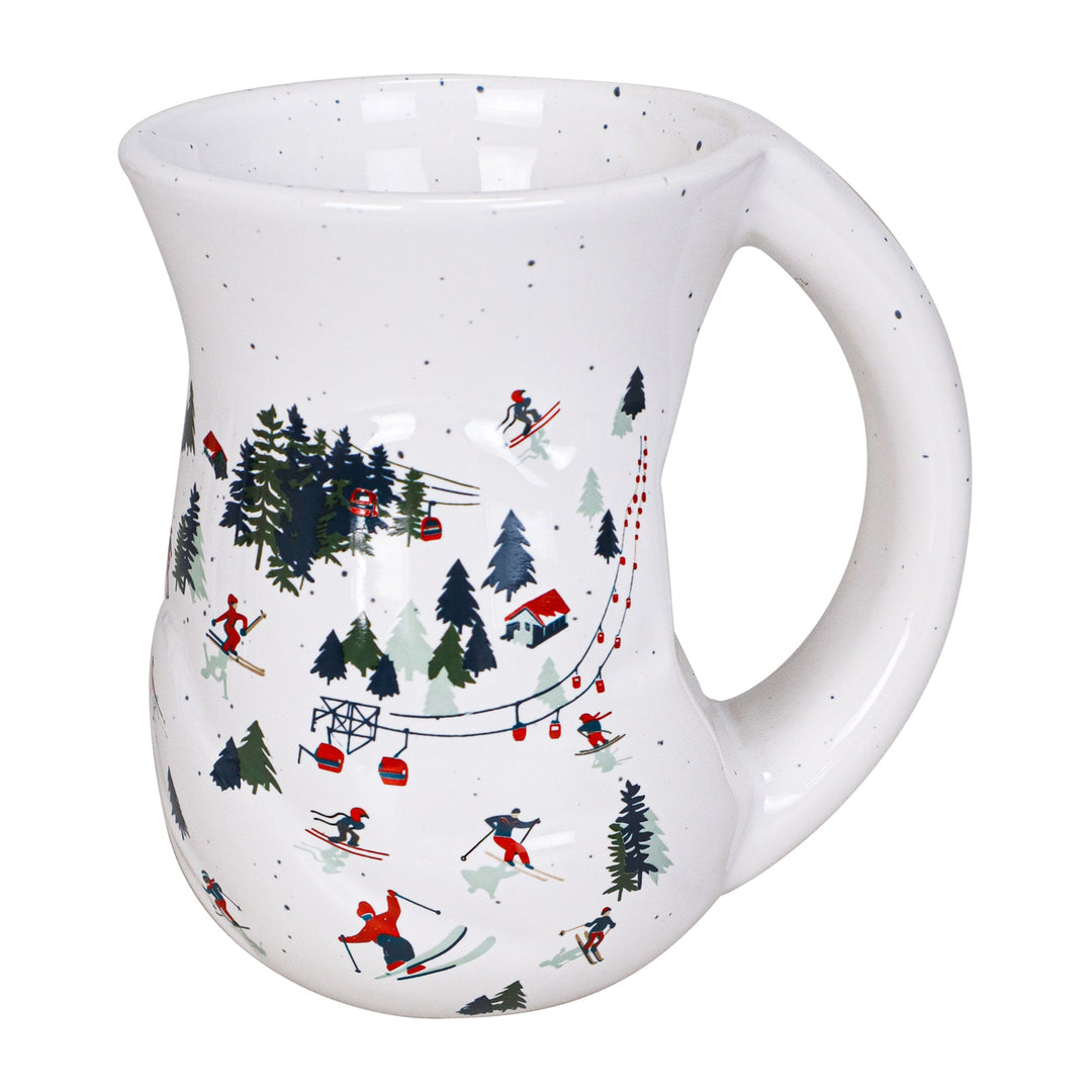 A white ceramic mug with a ski resort pattern featuring skiers, pine trees, lifts, and red cabins, shown on a plain white background.