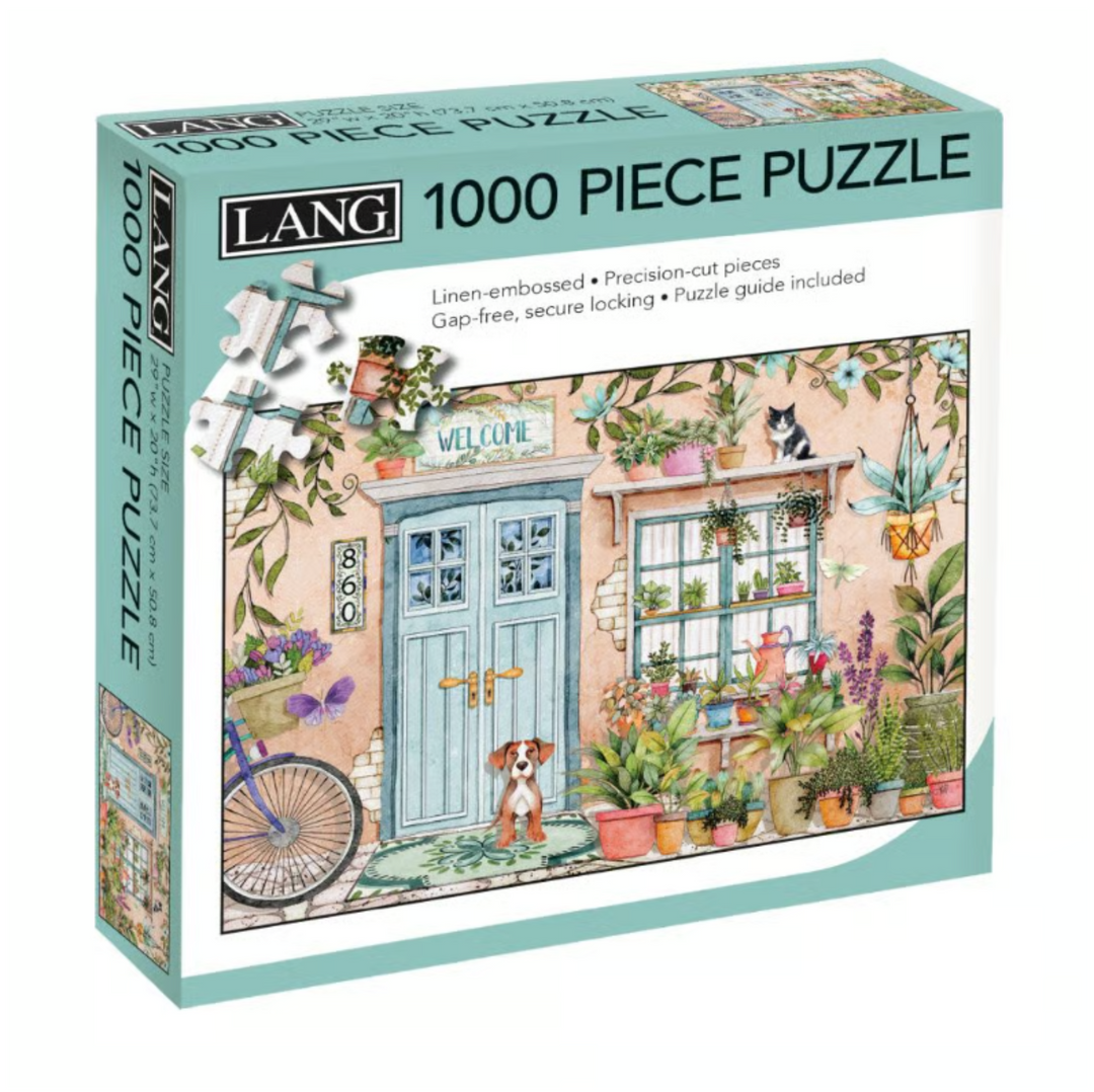 A Lang 1000-piece jigsaw puzzle box featuring a colorful illustrated garden and cottage scene with a blue door, potted plants, a bicycle, and a dog.