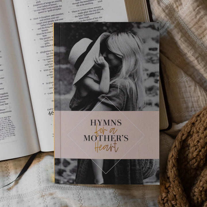 Book titled 'Hymns for a Mother's Heart' with a black and white photo of a woman on the cover, placed on an open book.