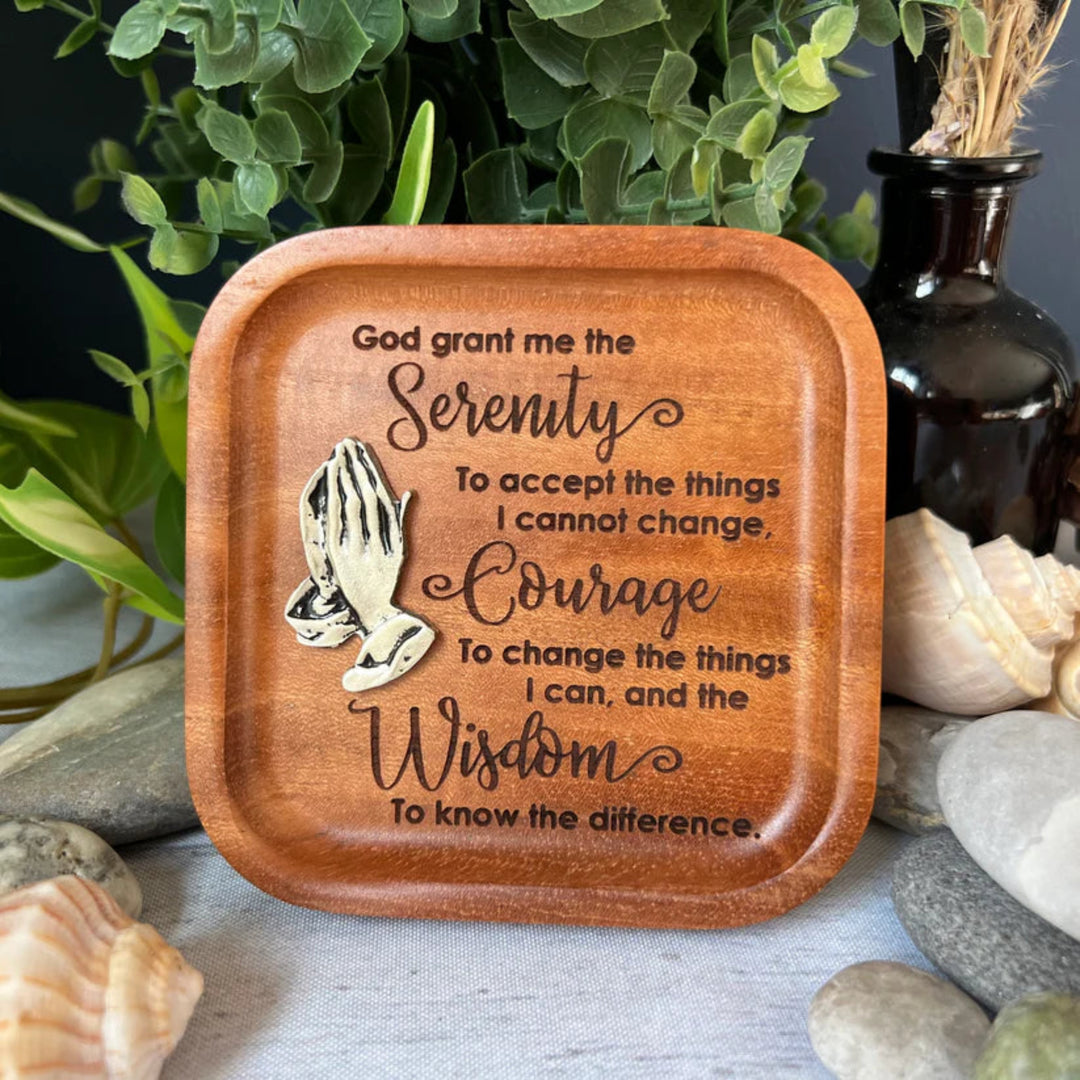 Wooden tray with engraved Serenity prayer on a natural setting with plants and stones.