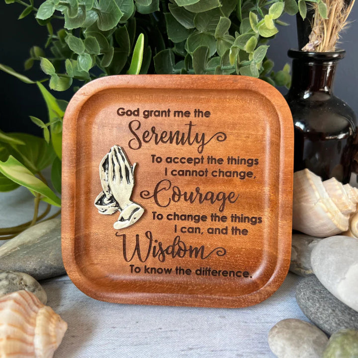 Wooden tray with engraved Serenity prayer on a natural setting with plants and stones.