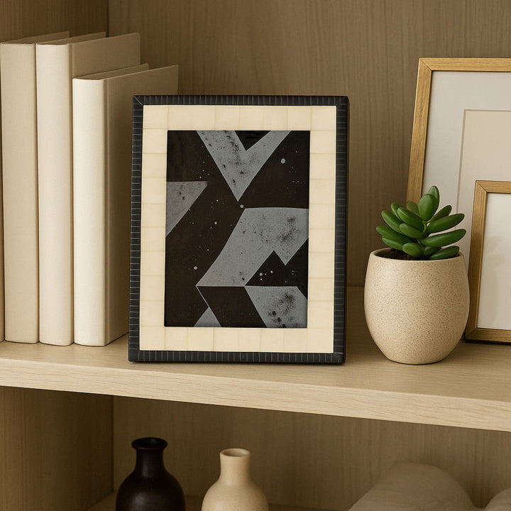 Framed abstract art on a shelf with books and a plant