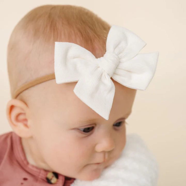 Baby wearing a white bow headband against a beige background