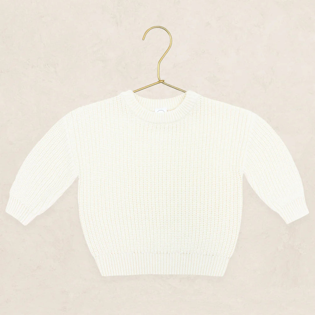 An off-white ribbed knit sweater with three-quarter sleeves, displayed on a gold metal hanger against a textured beige background.