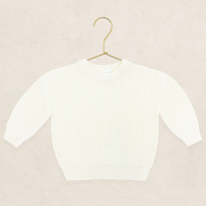 An off-white ribbed knit sweater with three-quarter sleeves, displayed on a gold metal hanger against a textured beige background.