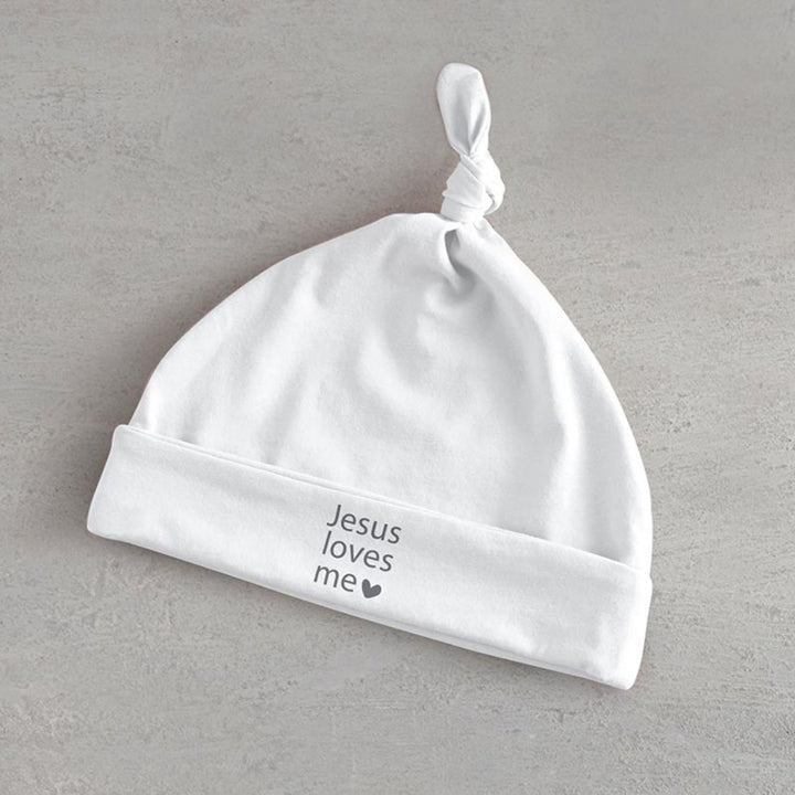 White baby hat with 'Jesus loves me' text on a gray background