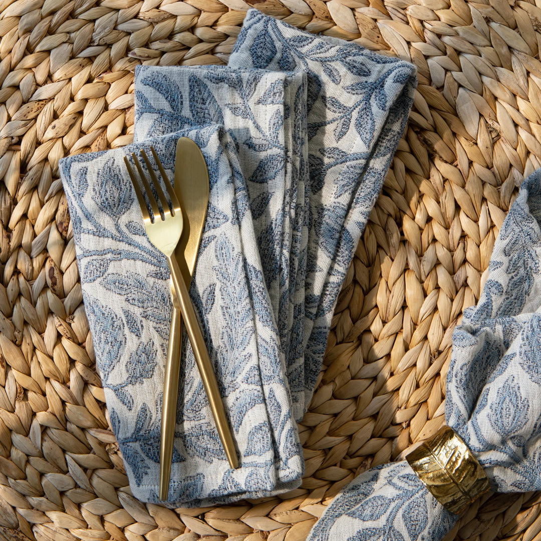 Larkspur Topiary Napkin with gold silverware and on a rattan placemat